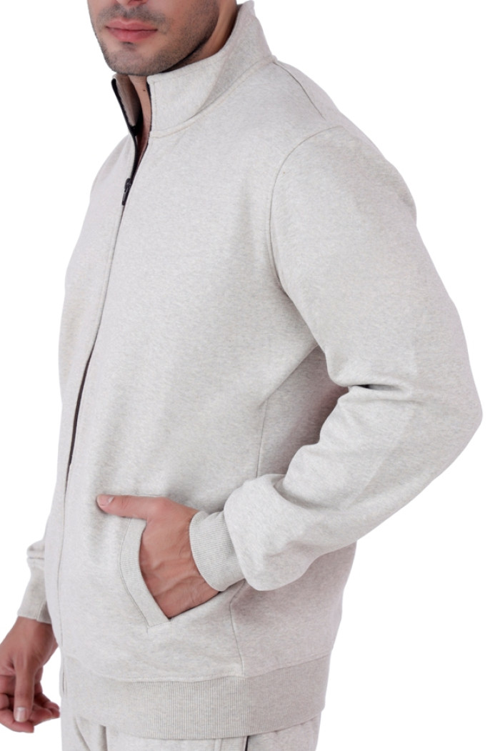 Close-up side view of a man wearing a Turfit’s Oatmeal Millage zip-up tracksuit jacket with a high collar and hand placed in the front pocket, showing fabric texture and stitching details.